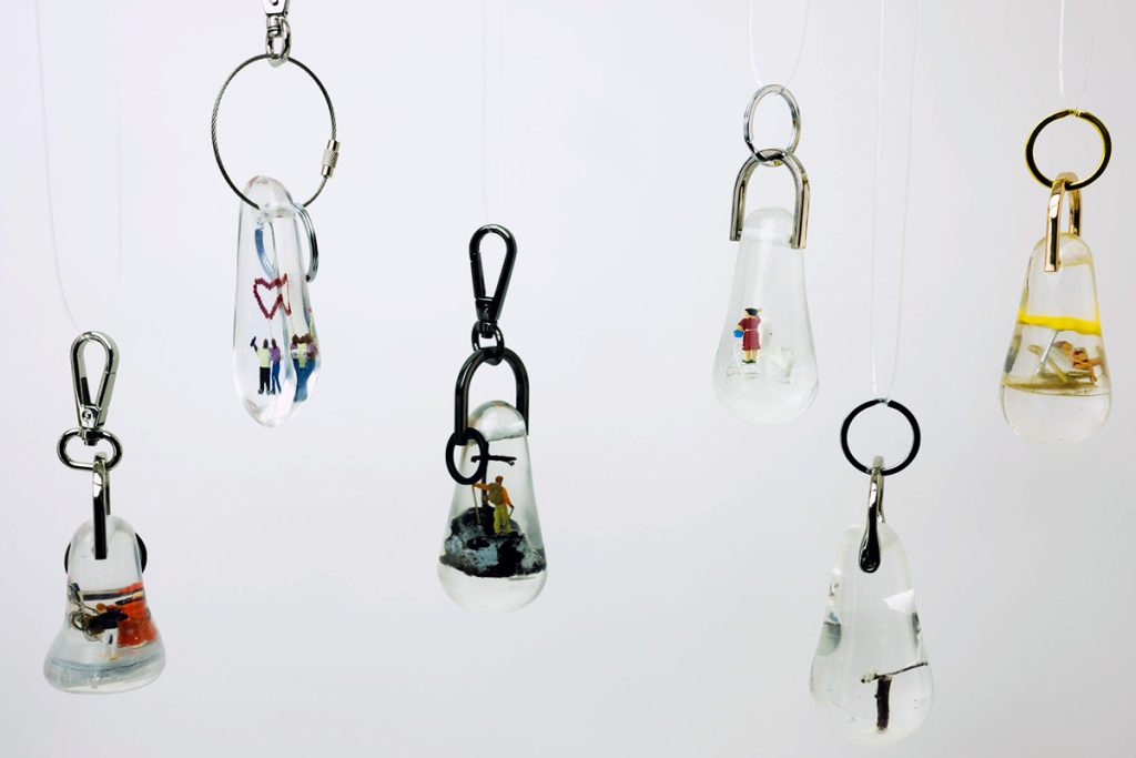 6 Schlüsselanhänger aus Epoxidharz aus der Serie "Schlüsselszenen" hängen frei schwebend.