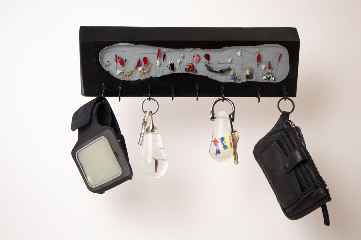 Schwarzes Schlüsselbord mit verschiedenen Gegenständen dranhängend, darunter Schlüsselanhänger der Serie "Schlüsselszenen"